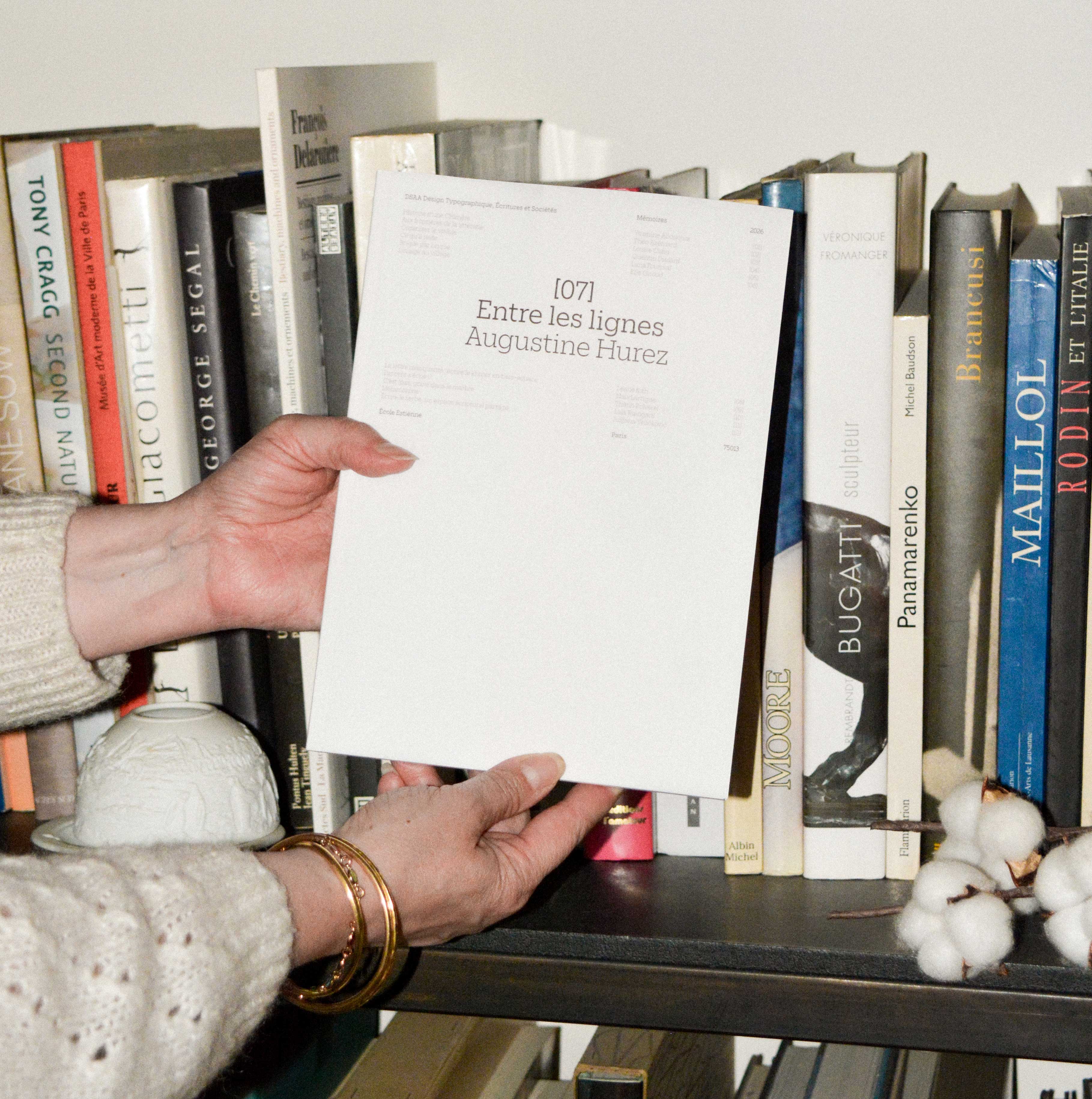 Une personne tenant le mémoire sur fond d'une bibliothèque, vue sur la couverture 